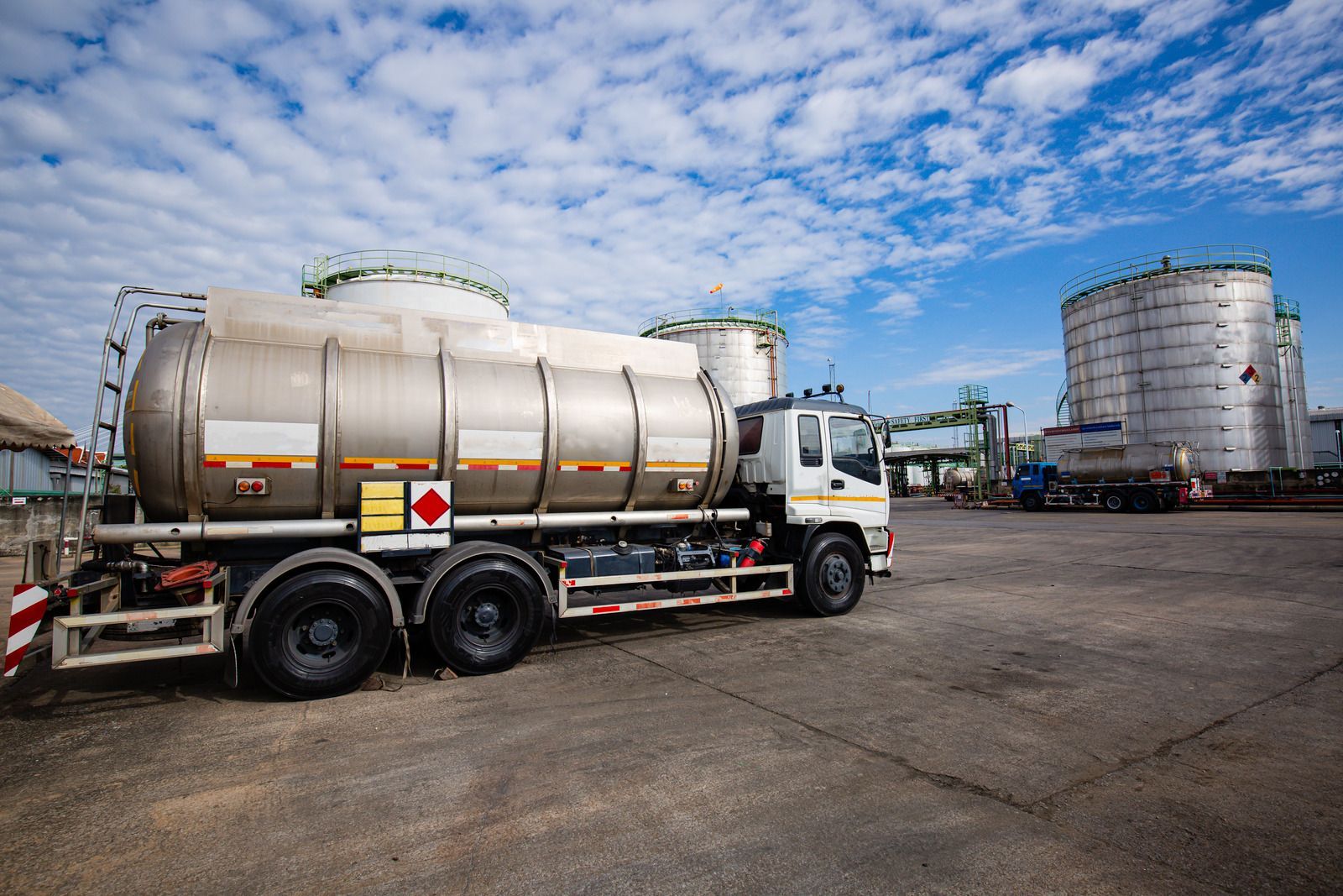 A tanker truck is parked in a parking lot in front of a large tank.