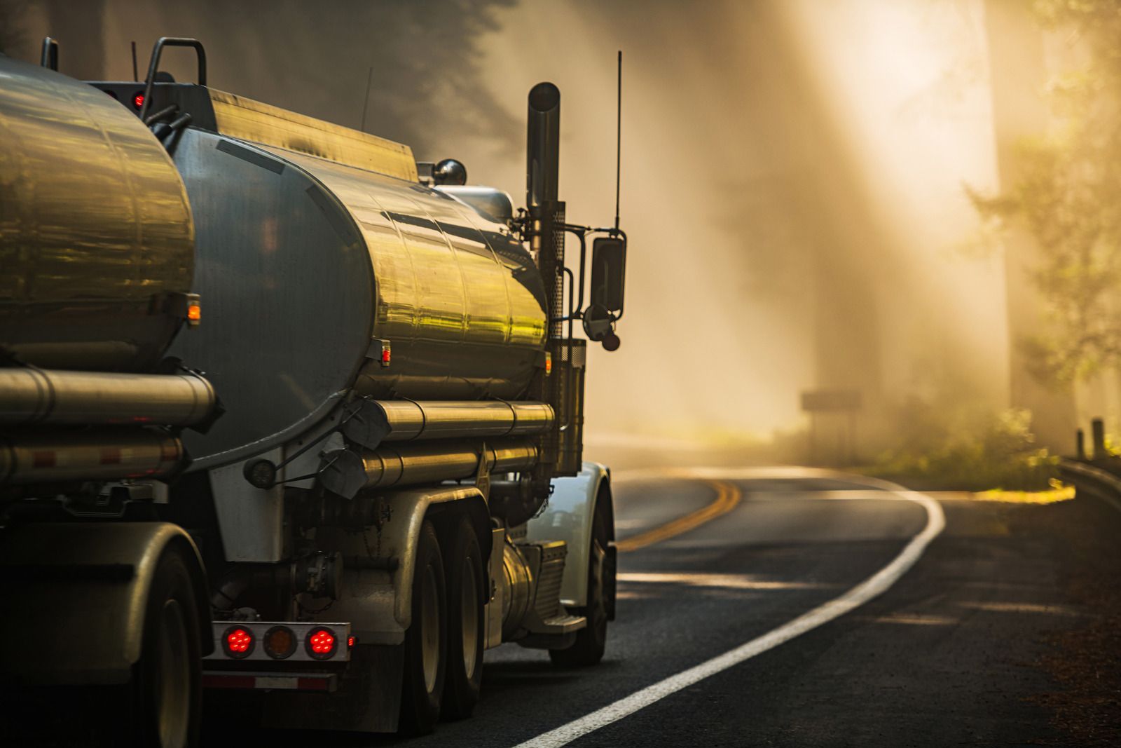 A tanker truck is driving down a curvy highway.