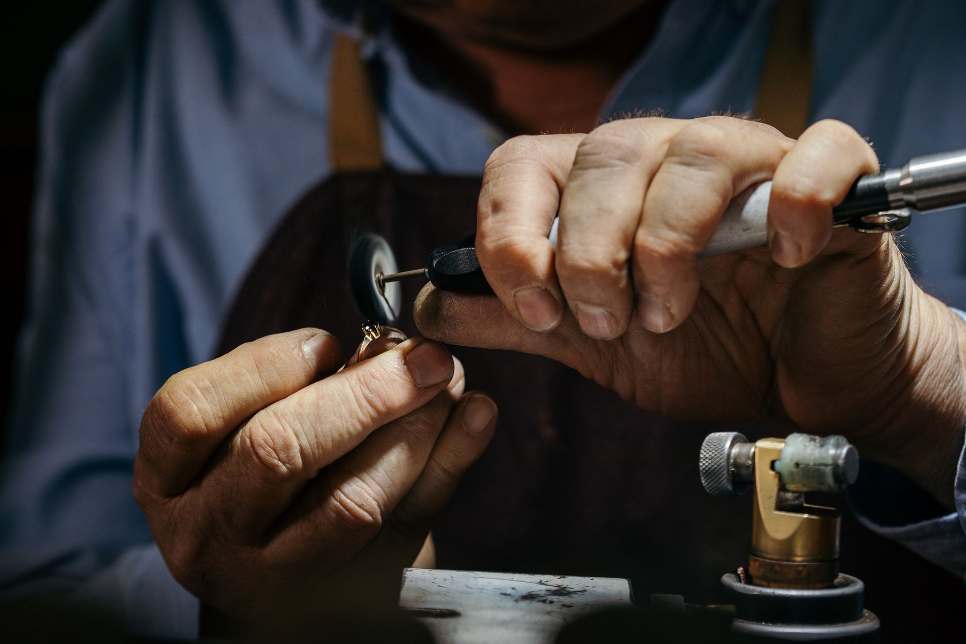Un gioielliere che lucida un gioiello con uno strumento portatile, indossando un grembiule, in un laboratorio.