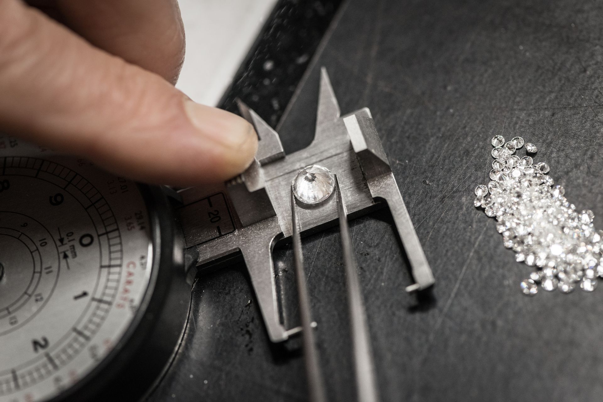Un gioielliere misura un diamante con un calibro: piccoli diamanti ammucchiati su una superficie scura.