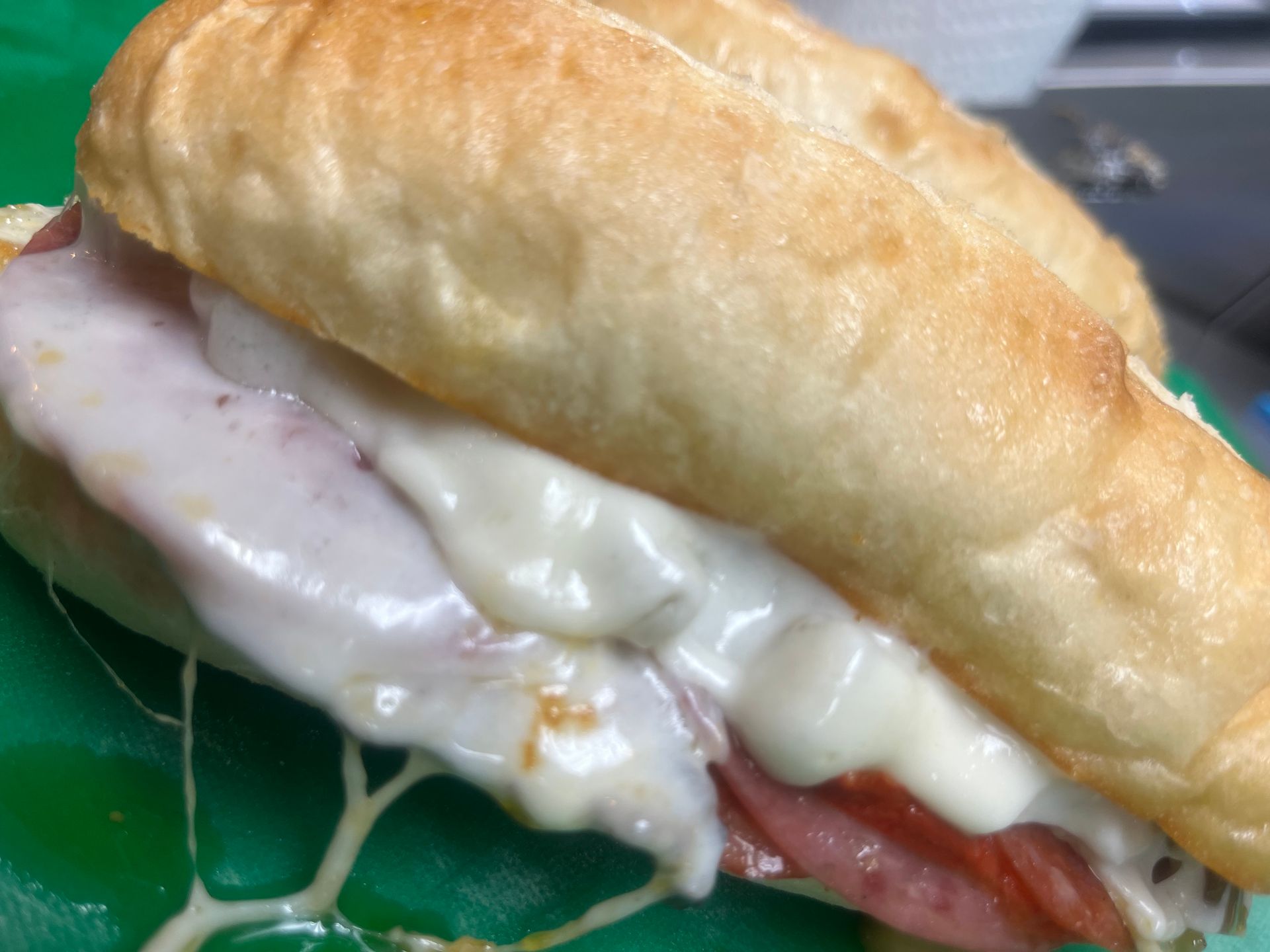 Close-up of a sandwich with melted cheese and meat on a green surface