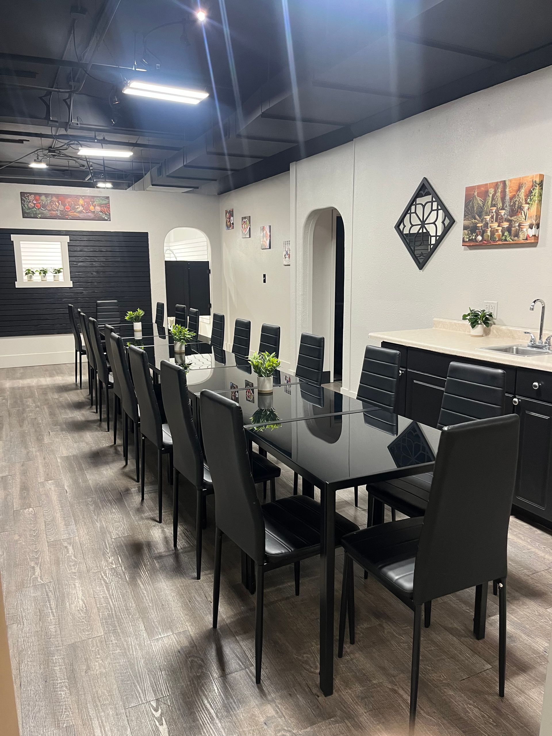 Empty dining area with black tables and chairs beside a long white wall under bright ceiling lights
