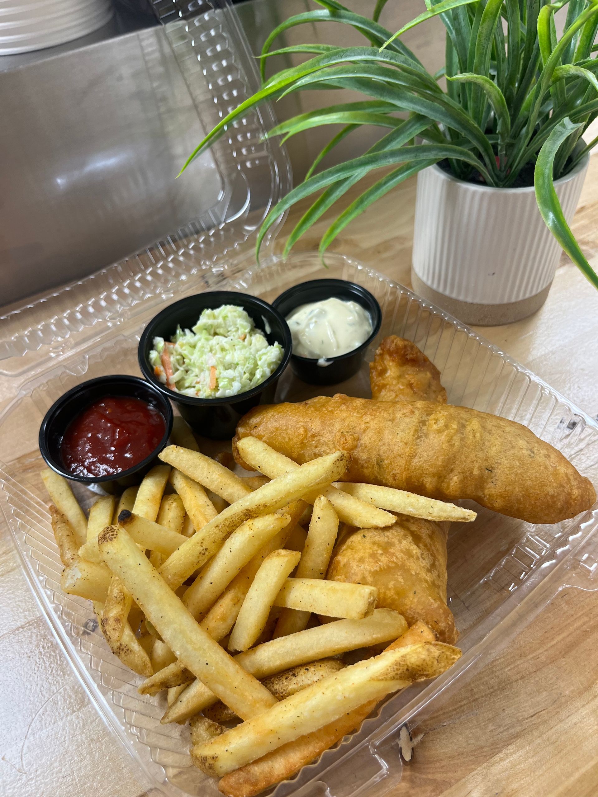 Takeout fish and chips with fries, slaw, ketchup, and tartar sauce on a table
