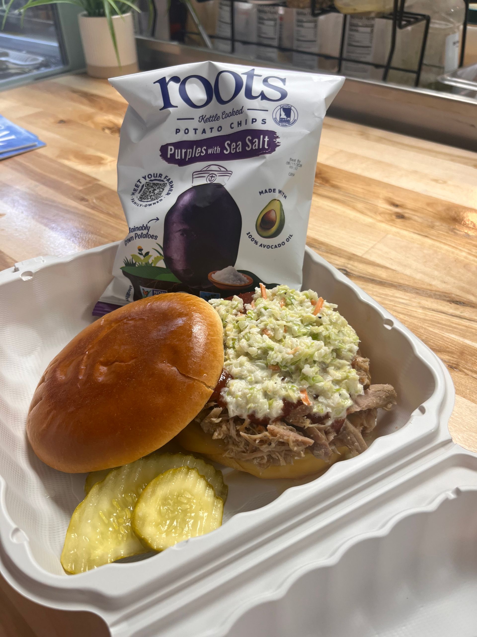 Takeout meal with sandwich, chips, and a bag of Toots Purple Sweet Potato chips on a table