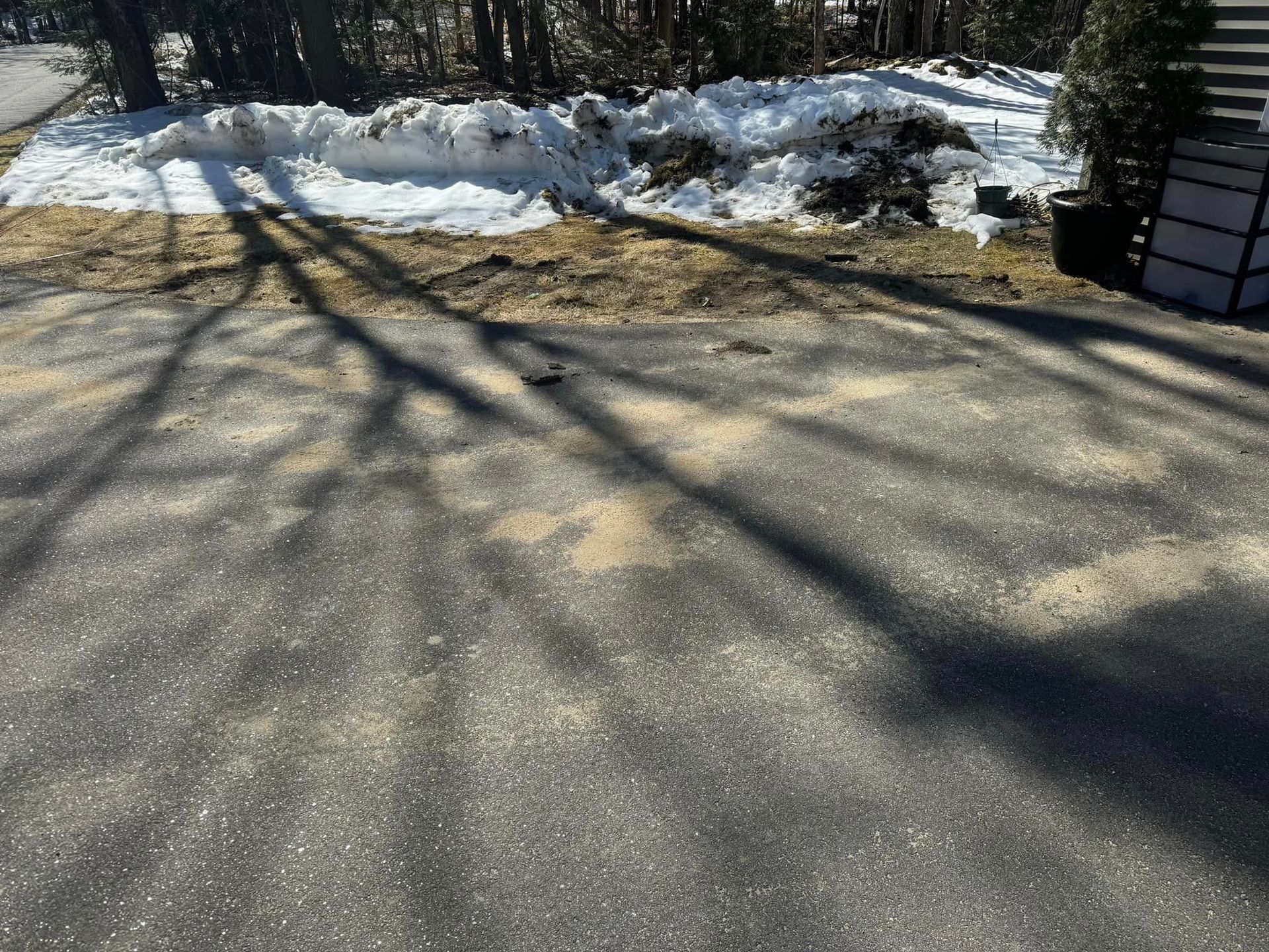 Snow-lined roadside beside a paved path with long tree shadows in bright sunlight