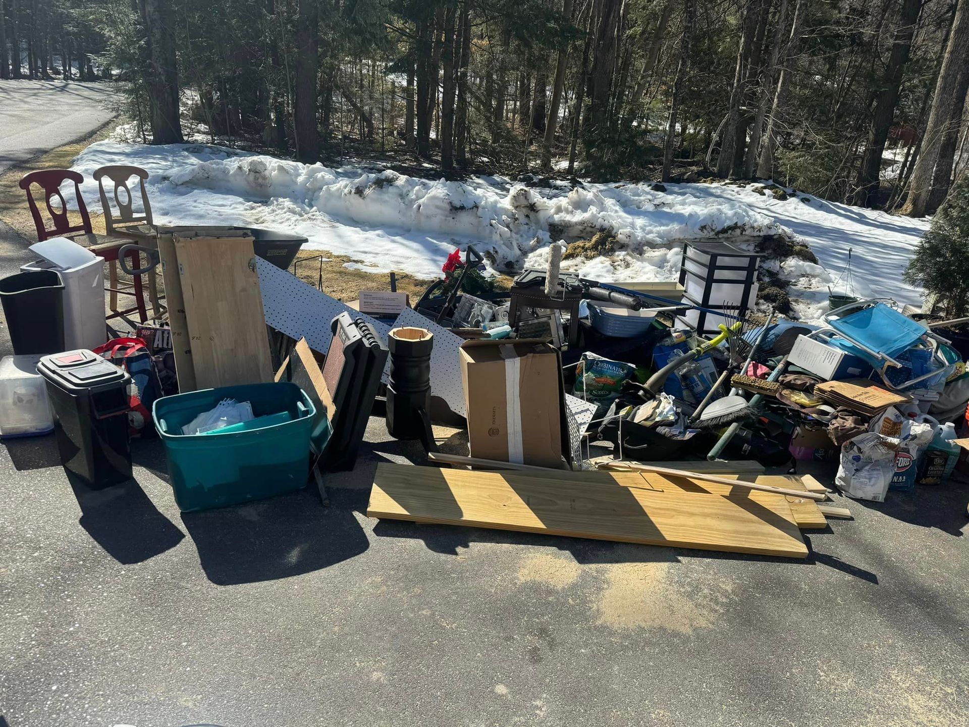 Piles of discarded furniture and trash on a roadside beside snow and trees