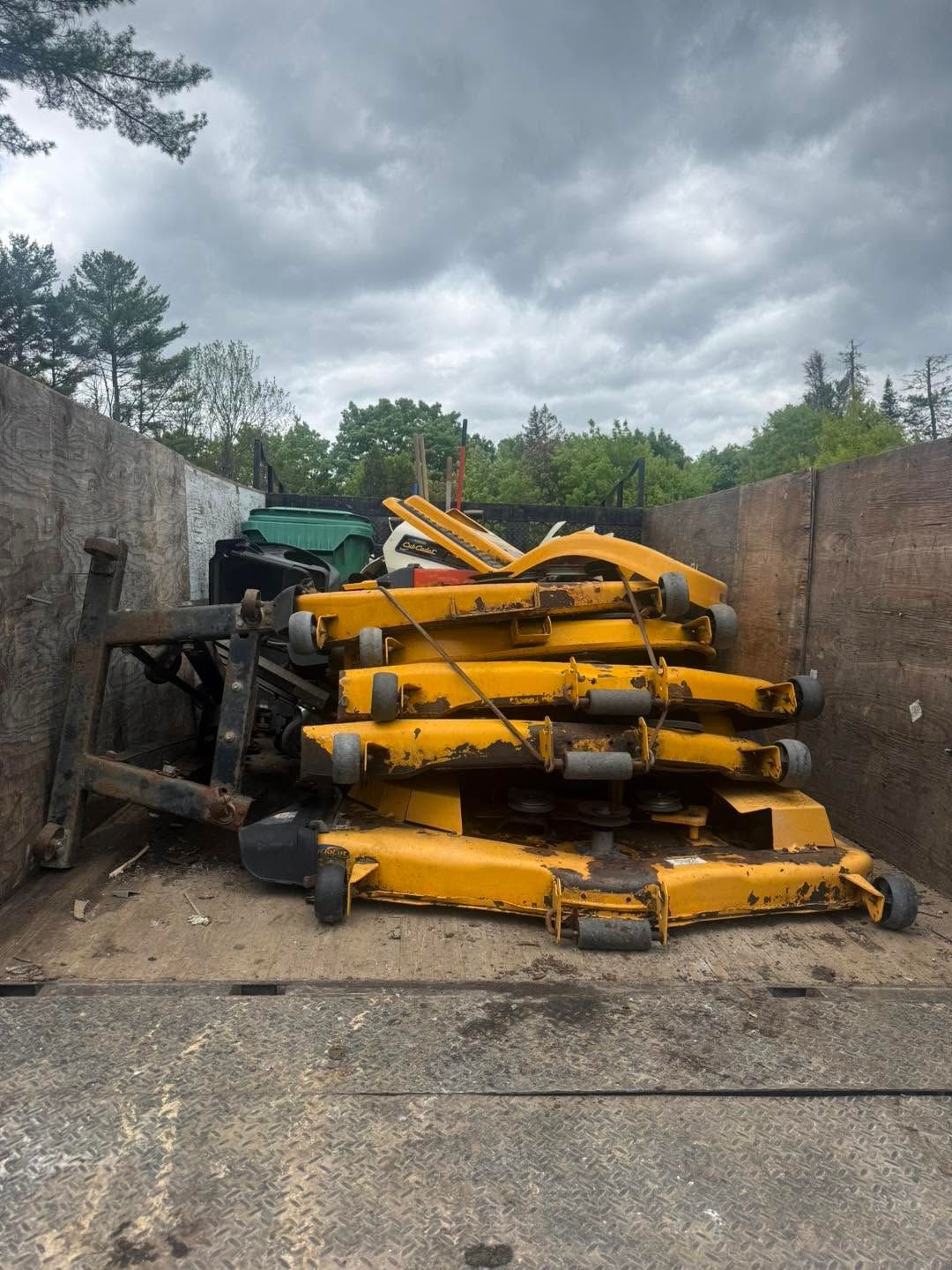 Stacked yellow industrial machine parts in a concrete yard beside high walls under a cloudy sky