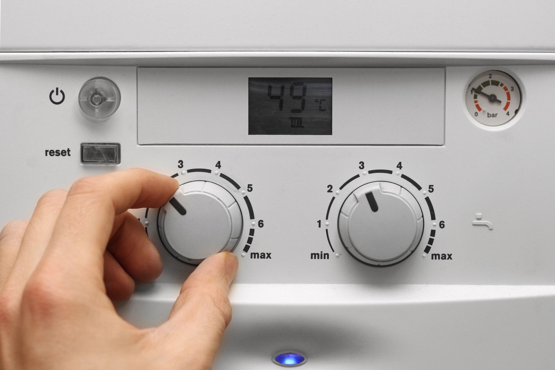 Mano che ruota una manopola bianca di controllo della caldaia su un pannello di riscaldamento a parete con display digitale e indicatore.