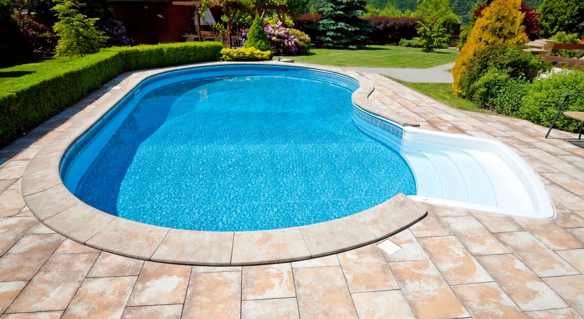 Piscina curva nel cortile sul retro con acqua azzurra, patio in pietra e verdeggiante paesaggio circostante.
