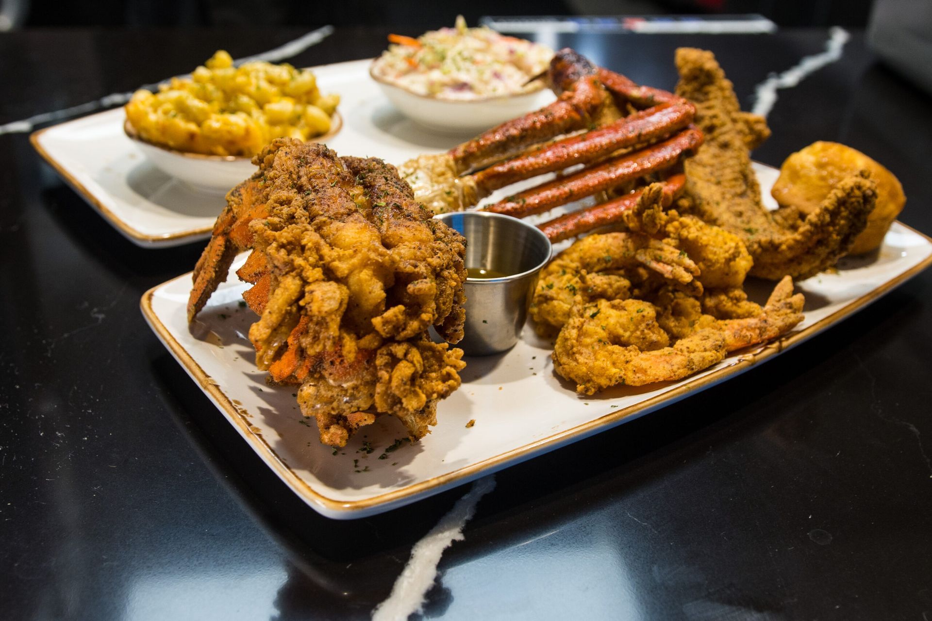A seafood platter featuring a fried lobster tail, crab legs, shrimp, and fish served with sides on a dark table.