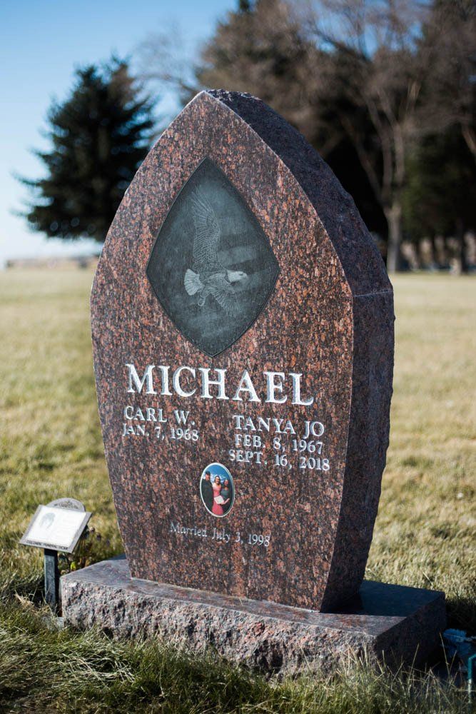 Dark granite headstone for Carl W. and Tanya Jo Michael featuring an engraved eagle and portrait