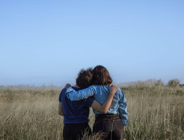 Two people standing in a field with an arm around each other in a comforting embrace