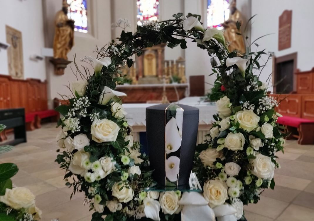 Cremation urn surrounded by a wreath of white roses and lilies at a funeral service inside a church.