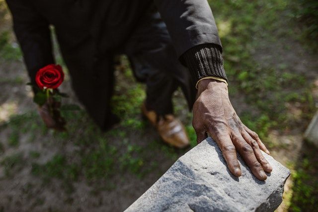 man softly touching cemetery headstone while placing a rose