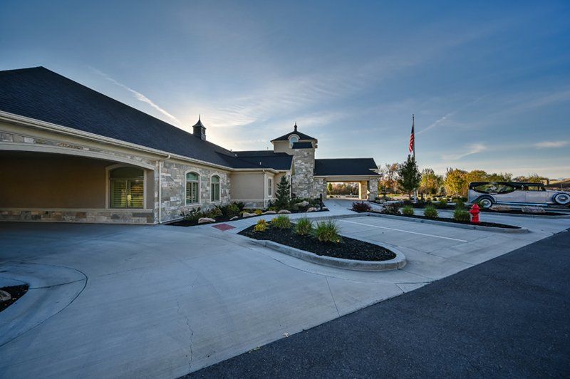 Exterior of White Pine Funeral Services in Logan, UT with covered entrance, American flag, and vintage Rolls-Royce inspired hearse