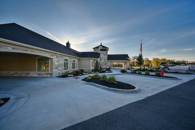Exterior of White Pine Funeral Services in Logan, UT with covered entrance, American flag, and vintage Rolls-Royce inspired hearse