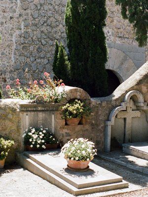 Peaceful cemetery scene with stone architecture, lush greenery, and potted flowers, symbolizing a place of remembrance and viewing obituaries.