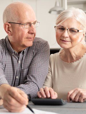 Elderly couple sitting together, reviewing documents and planning on a laptop, representing funeral pre-planning services.
