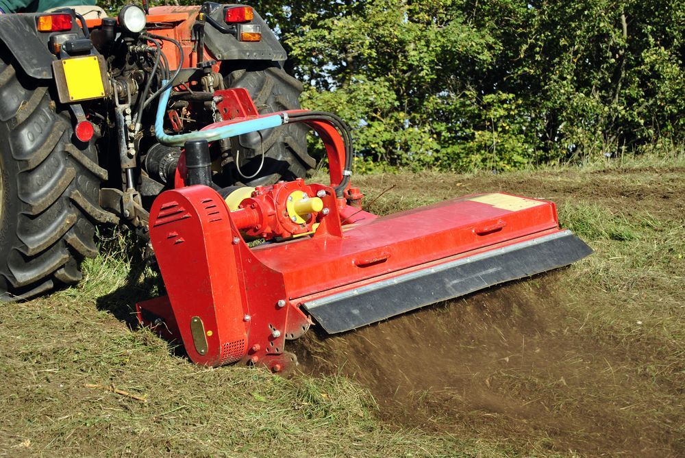 Red tractor using a rear flail mower to cut grass along a field edge
