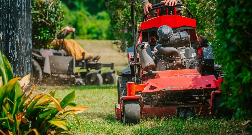 Two red lawn mowers cutting a grassy path, one in front with a driver and one in the background.
