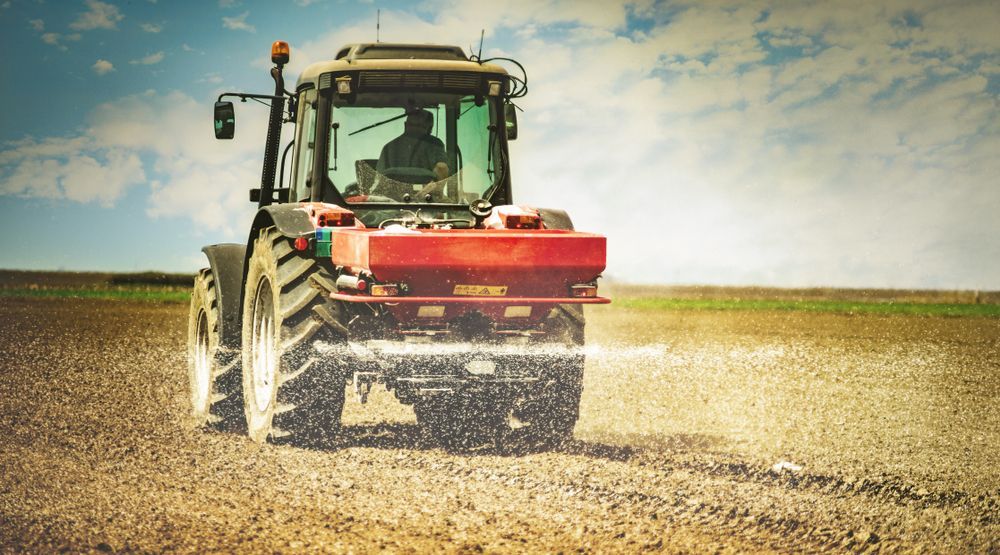 Red tractor spraying a field under a bright sky, with dust and crops visible in the background.