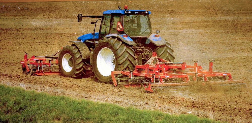 Blue tractor tilling a muddy field with red farm equipment