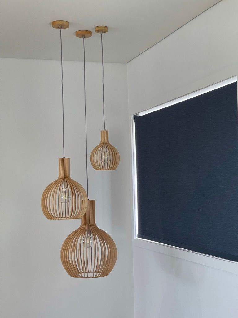 Three wooden pendant lights are hanging from the ceiling next to a window.