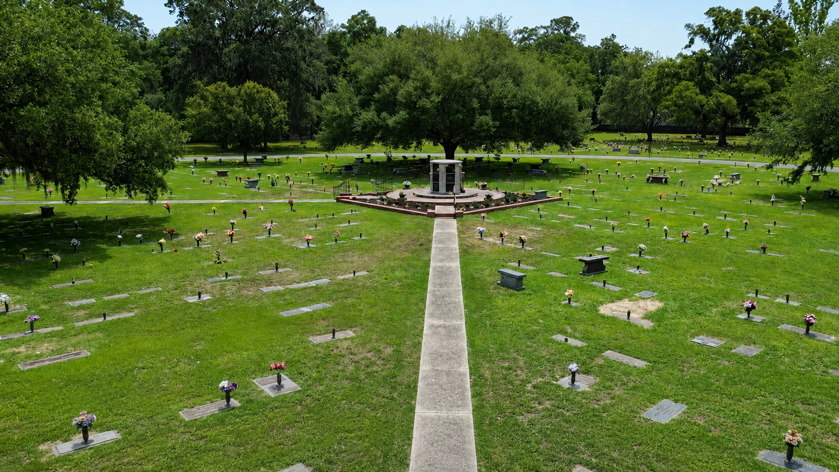 Mourners in black suits stand at a graveside with a white floral arrangement during a funeral.