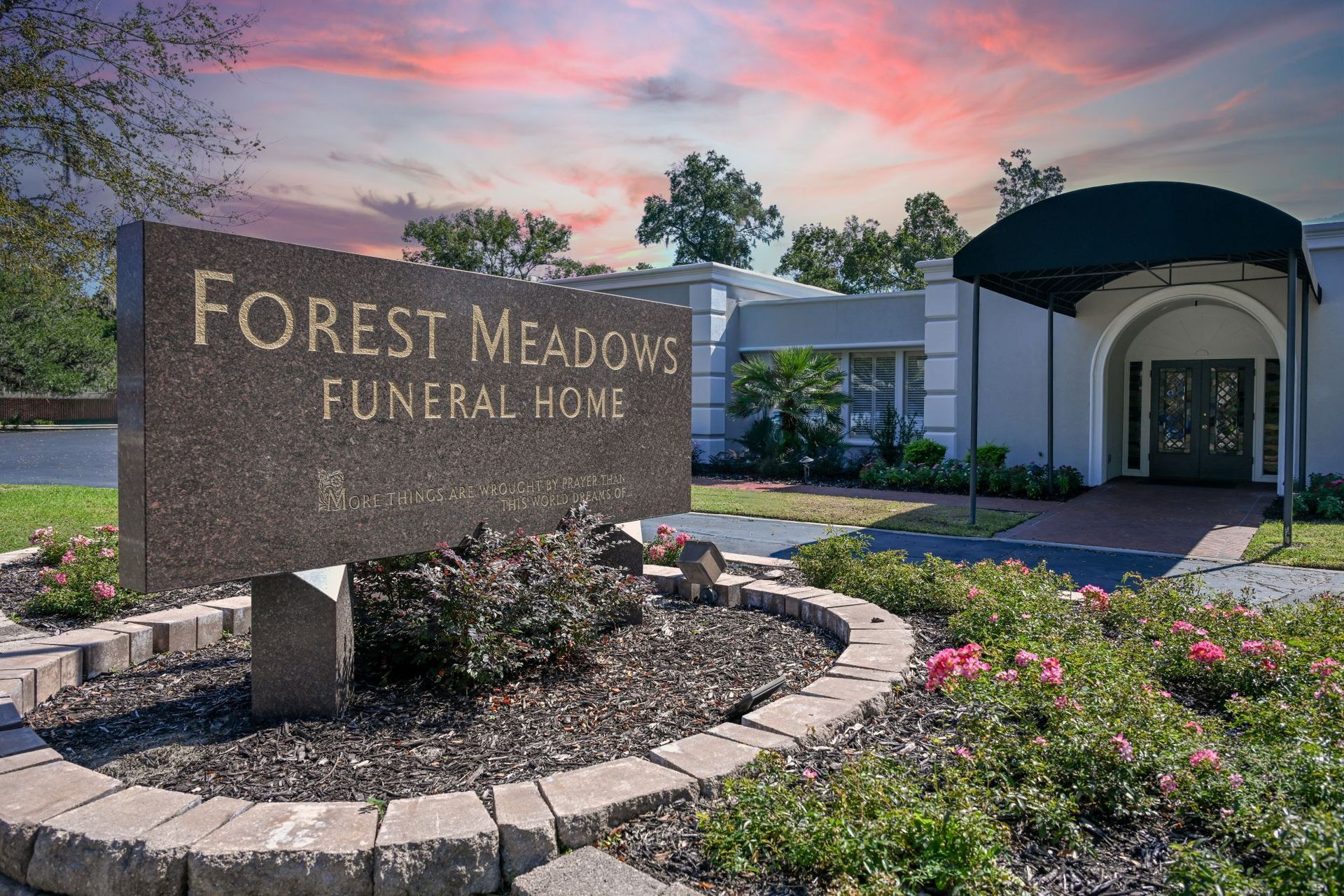 Forest Meadows Funeral Home sign by a landscaped entrance at dusk with pink clouds