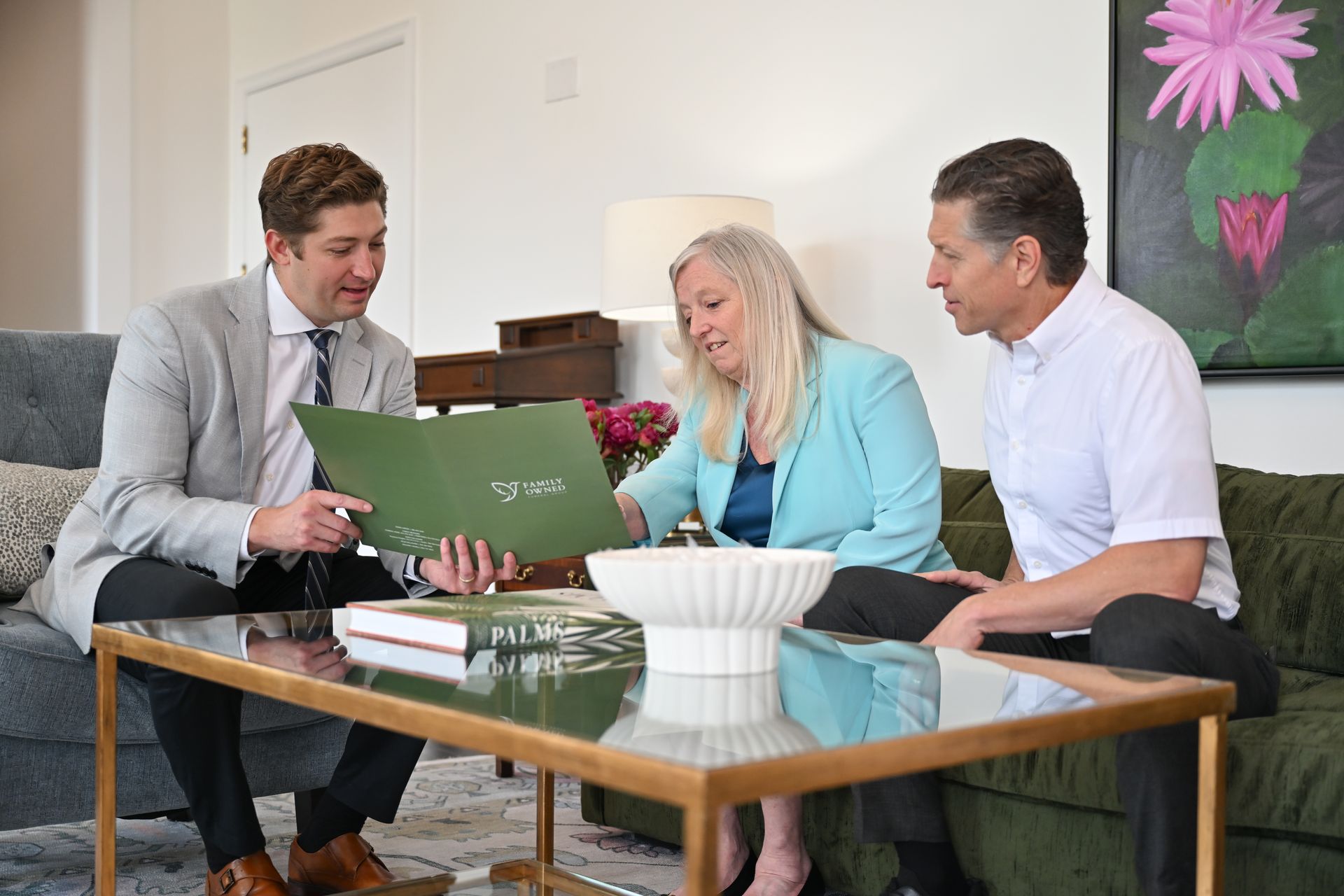 Three people sitting on a couch reviewing documents around a glass coffee table