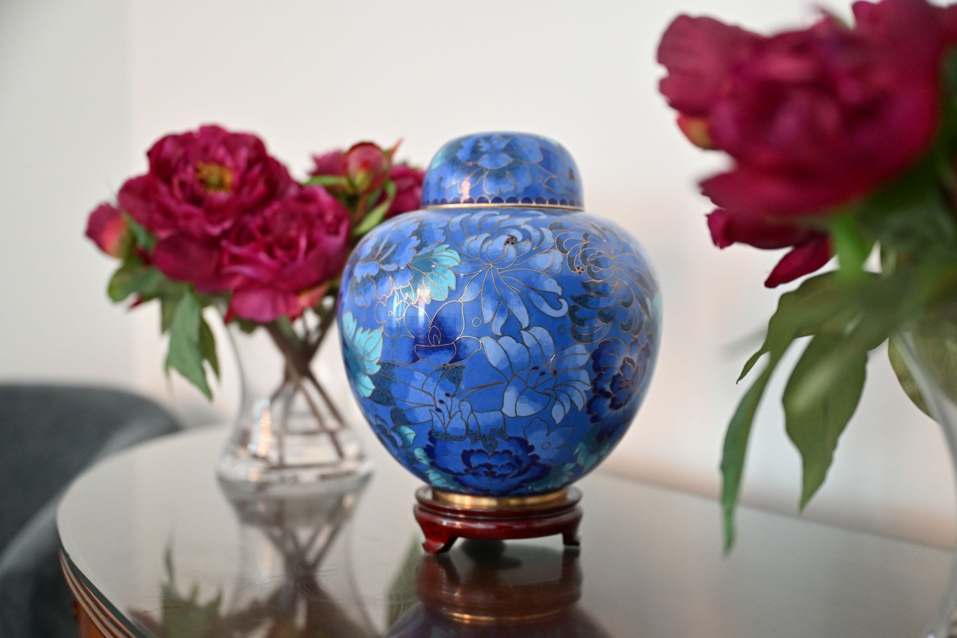 Blue floral porcelain jar on a glass table with pink flowers in the background