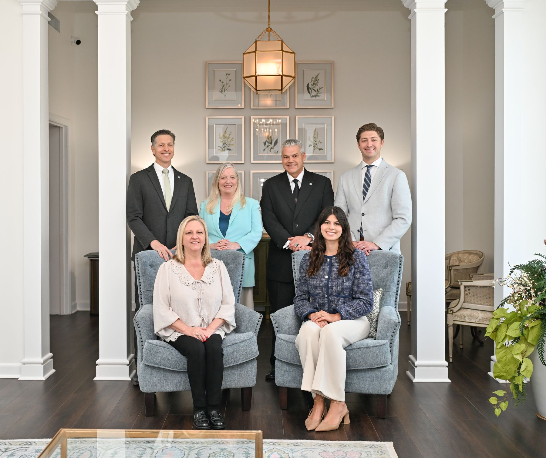 Six people posing in a bright living room with white columns and gray chairs.