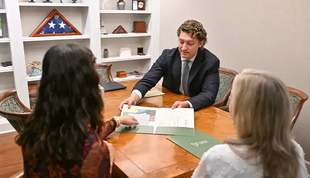 Three people in a meeting across a wooden table, reviewing documents in a small office.