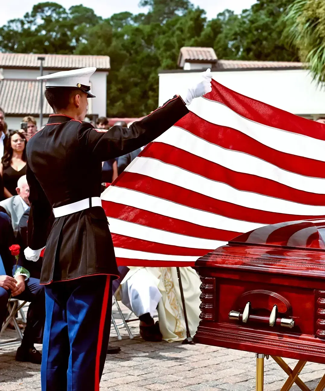 Uniformed guard holding a large American flag beside a polished red casket at an outdoor ceremony