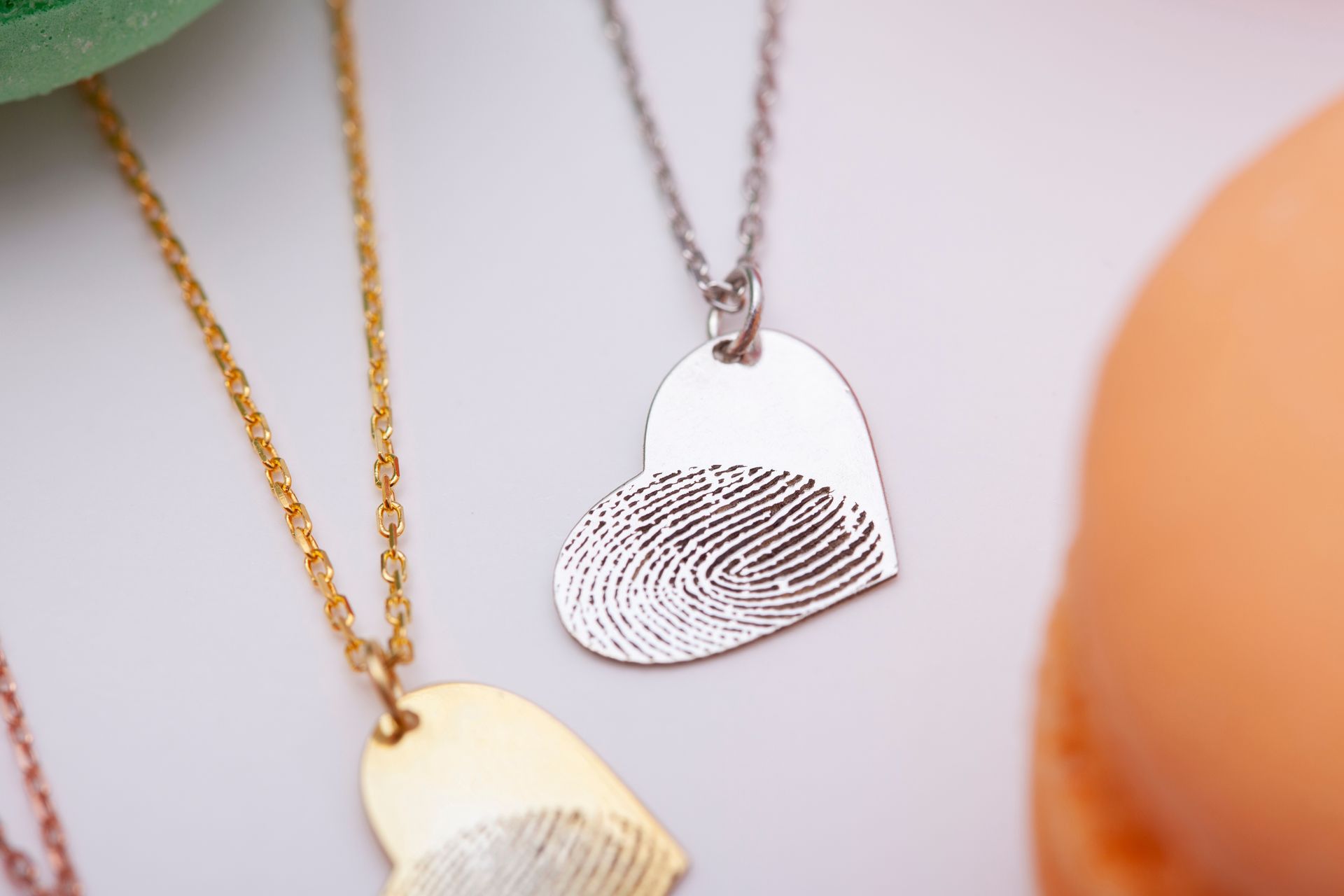 Two heart-shaped fingerprint necklaces in gold and silver, hanging on a light background