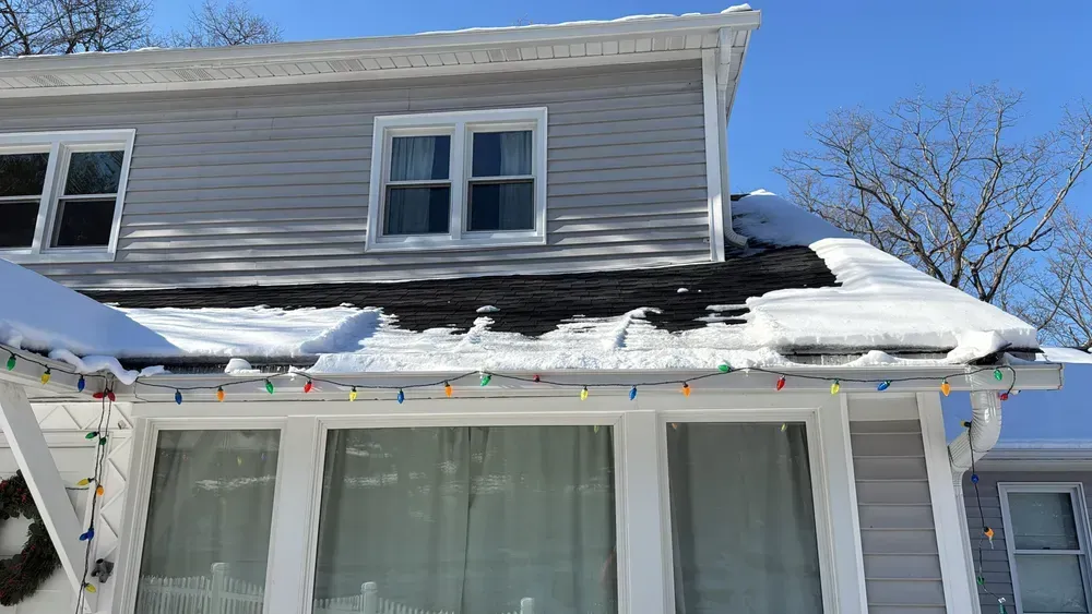 House roof with snow, Christmas lights, and a clear blue sky.