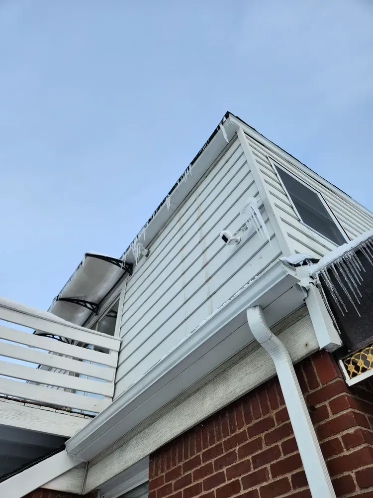 White house exterior with icy roof and gutters against a cloudy sky. Brick facade.
