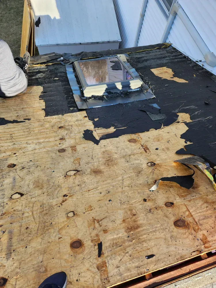 Rooftop with a skylight, showing exposed plywood with torn, black roofing material. Person visible.