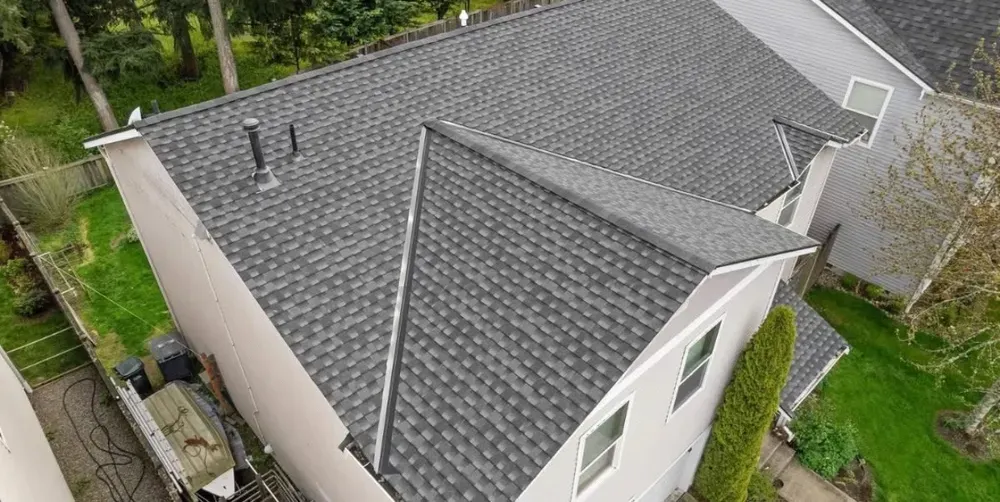 Overhead view of a house with a gray shingled roof, trees, and green grass.