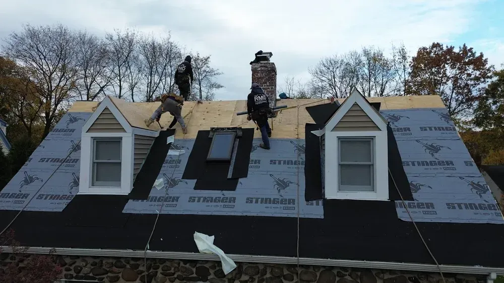Roofers working on a house roof, laying down new material on a cloudy day.