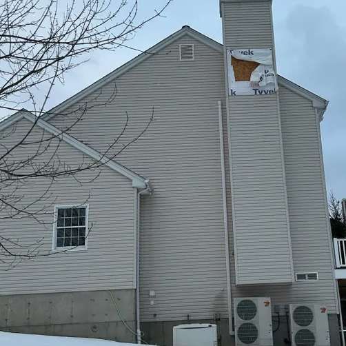 Side view of a house with light siding and chimney. Tyvek wrap exposed. Two AC units at base.