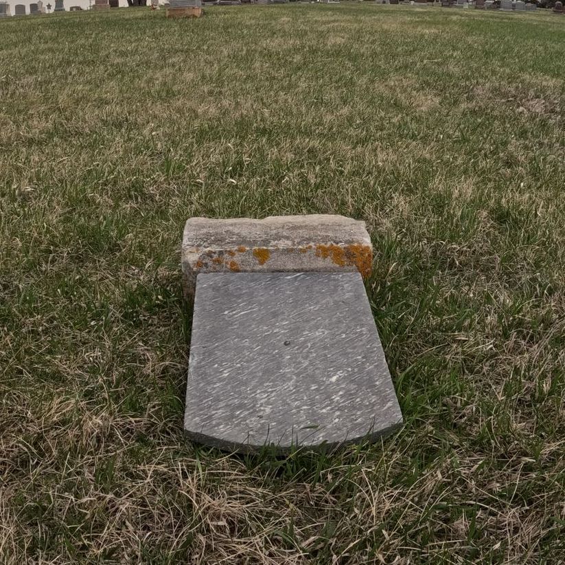A gravestone is laying in the grass in a cemetery.