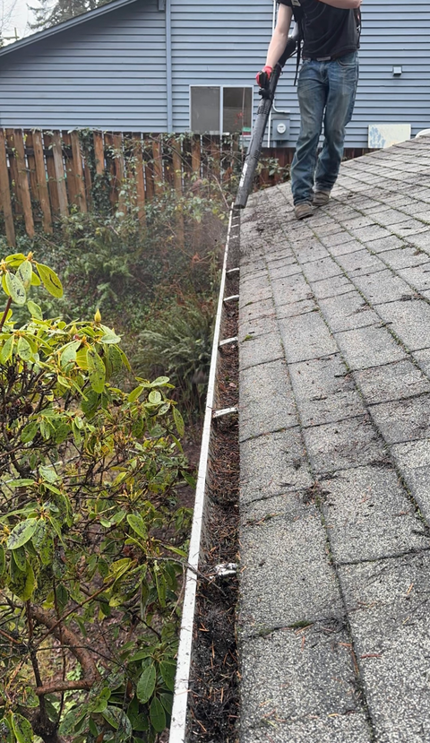 Person using a leaf blower on a roof, clearing debris from the gutter.