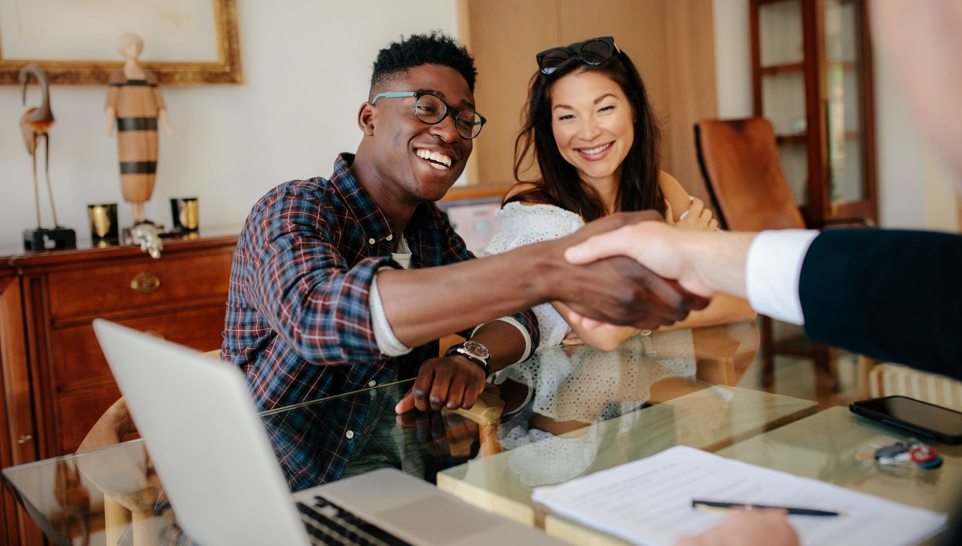 Couple shakes hands with a person, likely after a deal is finalized. They are smiling in a home office setting.