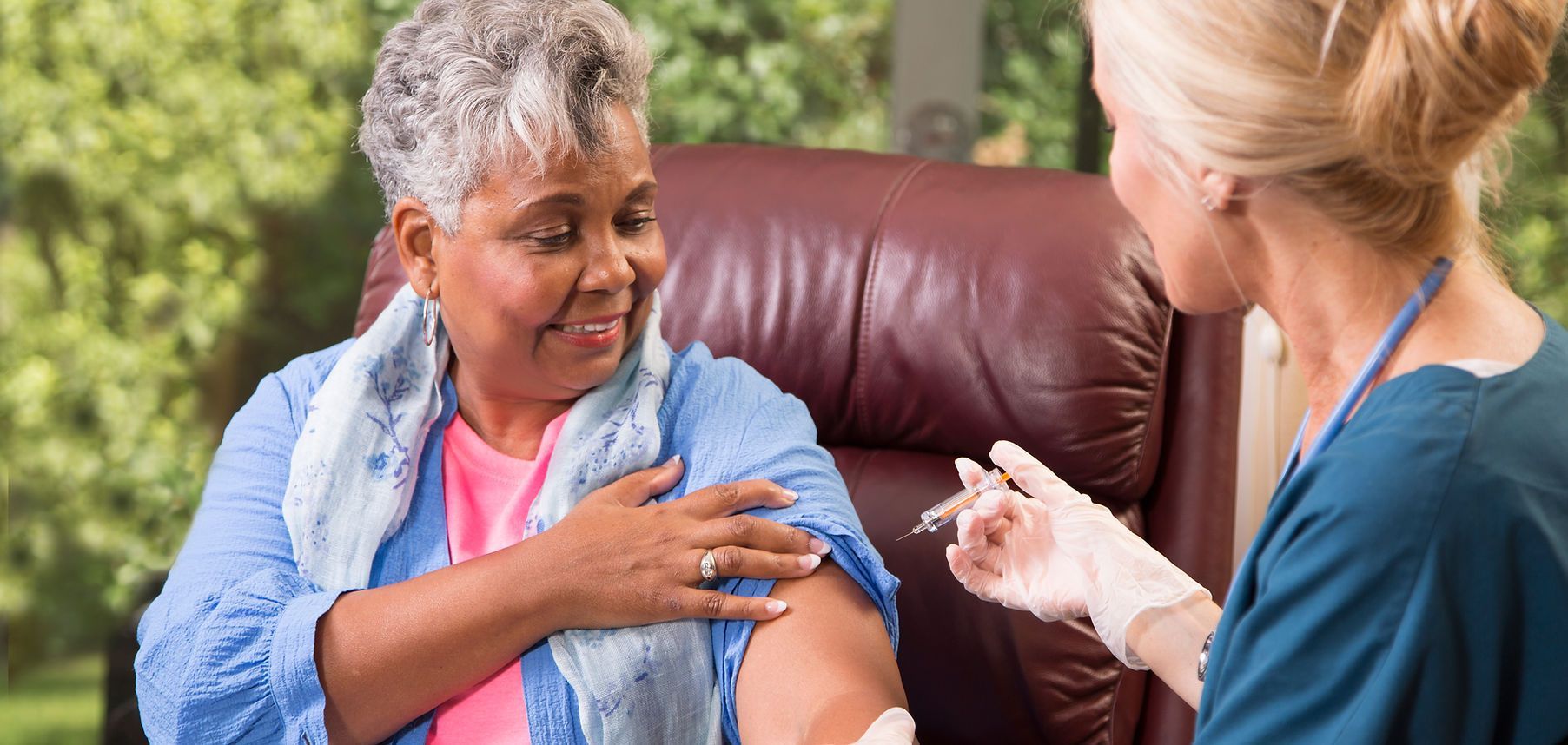 Nurse applies a bandage to a seated patient’s upper arm in a home setting.