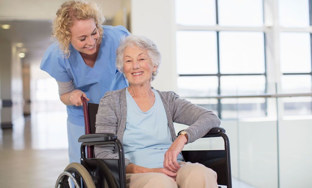 Caregiver helping a smiling woman in a wheelchair in a bright, modern room