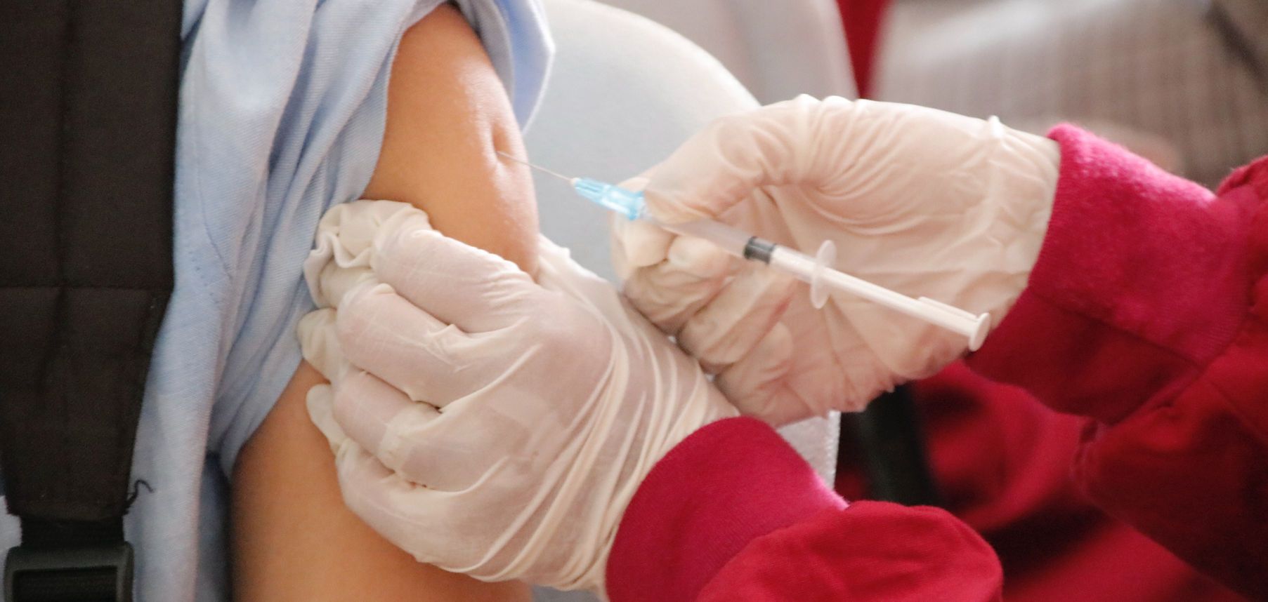 Gloved hands administer a vaccine injection into an arm with a blue sleeve