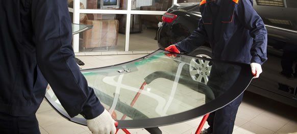 Two workers carrying a large curved glass pane indoors