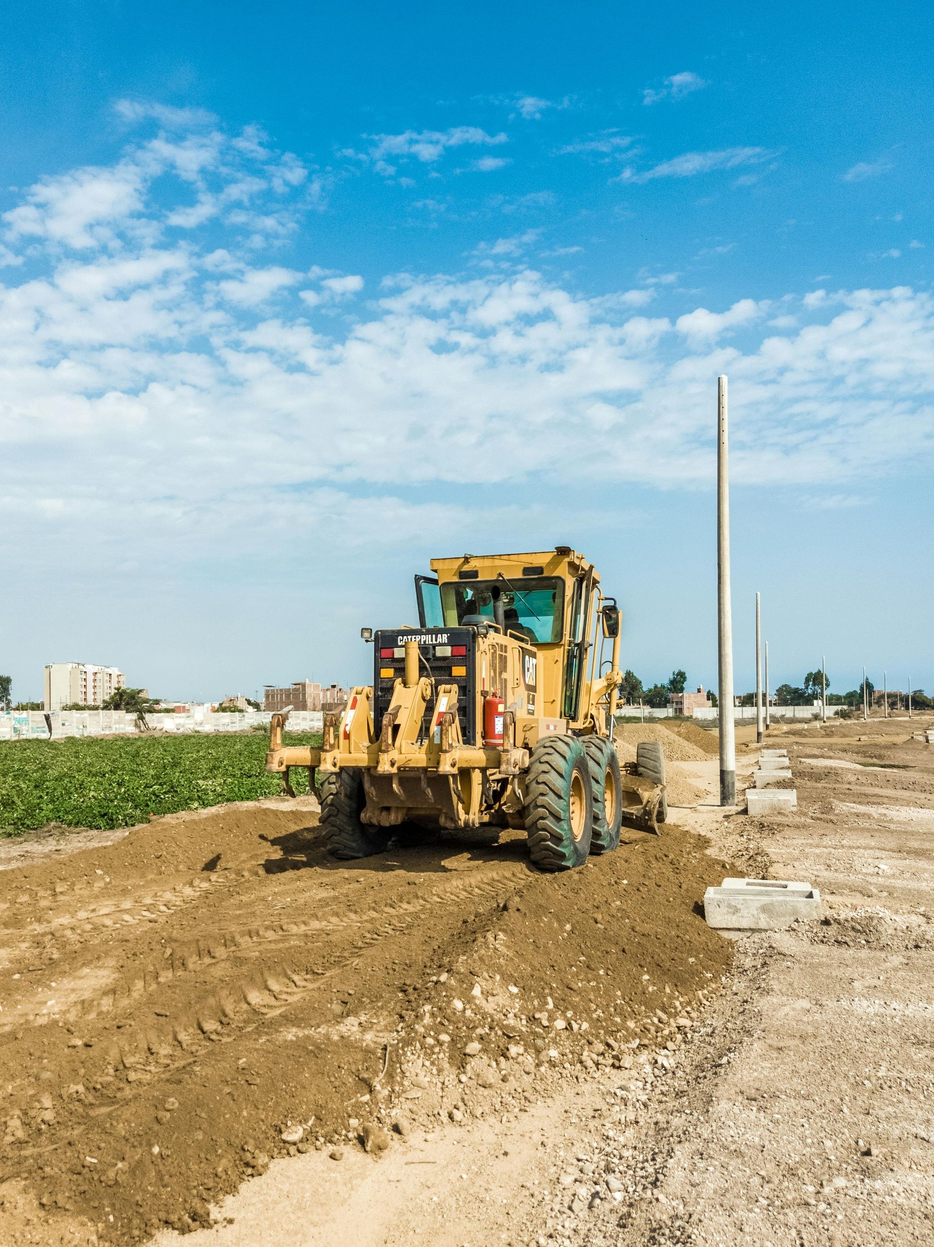 Yellow grader on a construction site, leveling dirt under a blue sky.