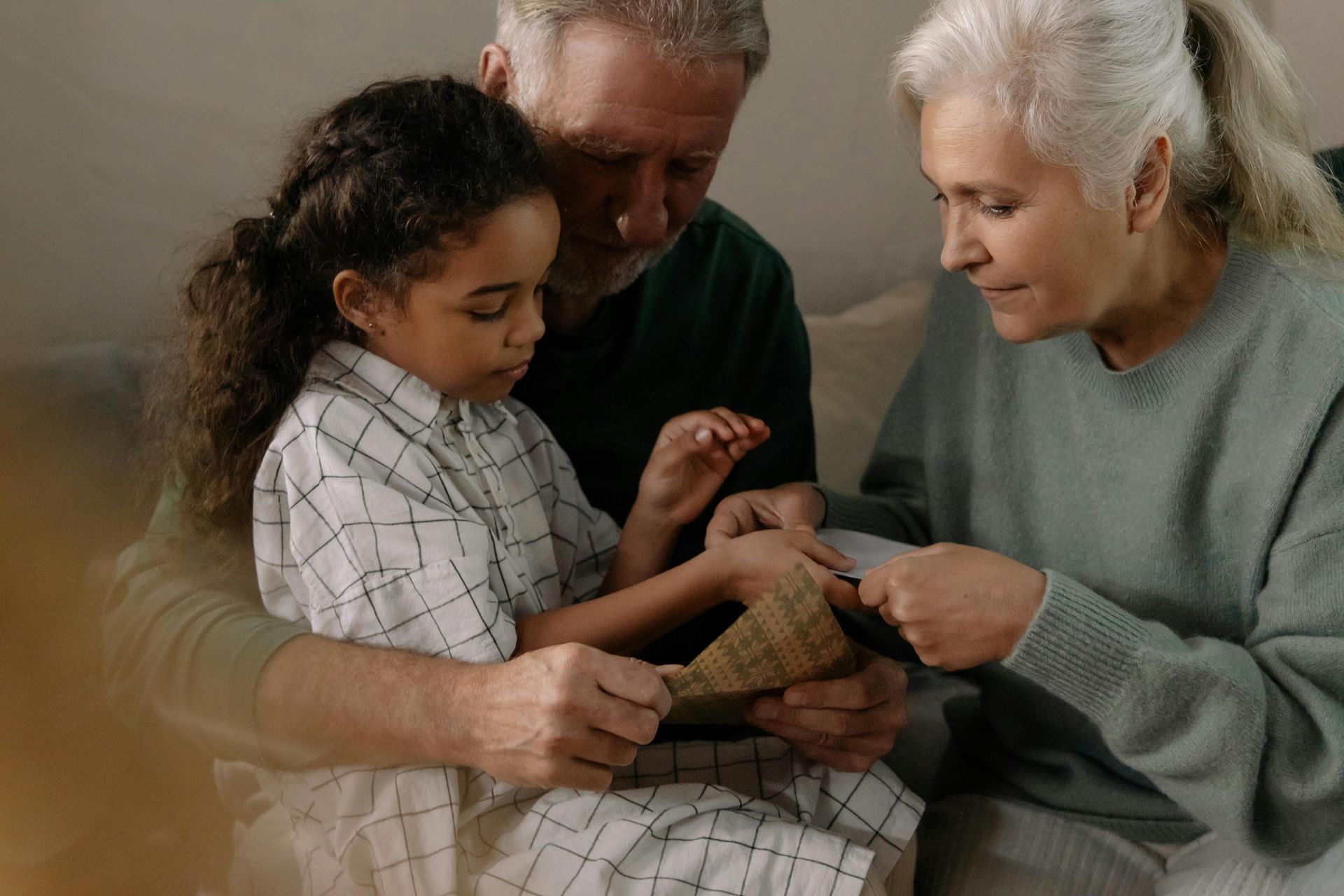 An elderly couple is sitting on a couch with a little girl.